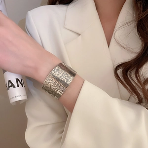 Detail of wide open bangle featuring irregular geometric texture on model in beige blazer