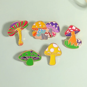 Set of five colorful enamel mushroom pins with glossy finish on a pale green surface