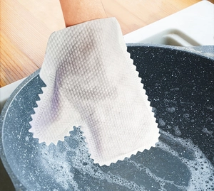 Macro view of white non-woven cleaning glove scrubbing a pan with soap foam bubbles