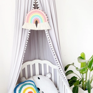 Detail of grey canopy with white pom pom tassels and handmade woven rainbow wall hanging