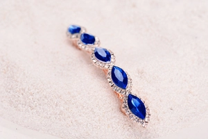 Close-up of rose gold hair clip featuring five blue gemstones and sparkling rhinestones