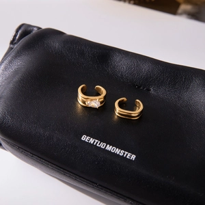 Detail of gold-plated drop zircon ear cuffs on luxury black leather texture background