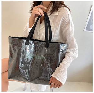 Detail of a large black glossy tote bag with Skillfully text carried by a model