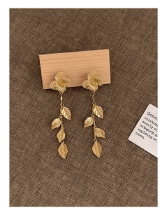 Détails des boucles d'oreilles fleurs et feuilles dorées sur présentoir en bois