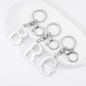 Polished stainless steel letter B, R, and G keychains with lobster clasps in a white tray