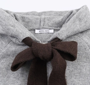 Detail of grey knitted hoodie with oversized brown bow and soft wool texture finish