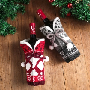 Red and grey knitted Christmas wine bottle covers with reindeer patterns on wooden table