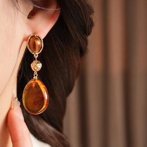 Detail view of amber resin teardrop earrings with golden accents worn by a model