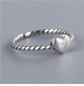Macro detail of silver twisted band ring featuring a minimalist heart center decoration