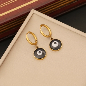 Golden hoop earrings with black evil eye pendants displayed on a beige leather pad