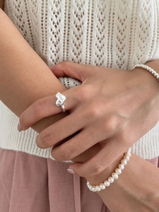 Detail of silver heart ring worn with pearl bracelet on minimalist knit background