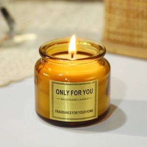 Handmade amber glass scented candle with cork lid and flickering flame on a white lace mat