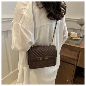 Detail of brown V-quilted leather crossbody bag with metal chain strap and decorative bar