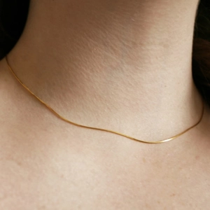 Close-up of minimalist thin gold snake chain necklace on woman's neck for elegant look