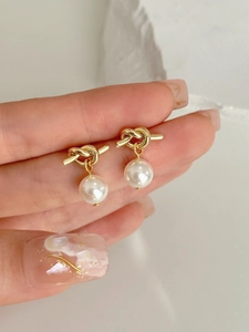 Close-up of golden knot stud earrings with elegant round white pearls held in hand