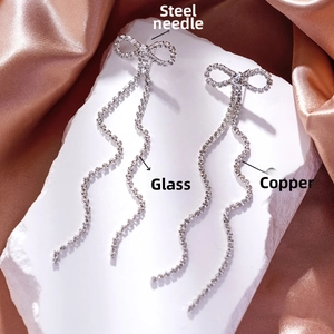 Detailed view of silver bow earrings with flowing crystal tassels on stone surface