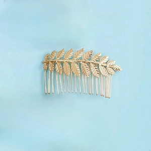 Golden leaf-shaped metal hair comb accessory for women on a solid blue background