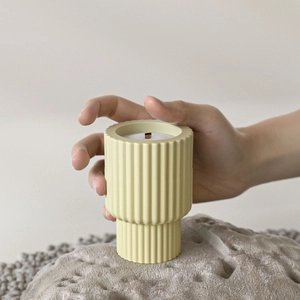 Detailed view of hand touching a yellow striped resin candle cup with a wooden wick