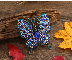 Détail de la broche papillon vintage dorée avec strass bleus sur feuilles d'automne