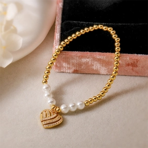 Gros plan du bracelet à perles dorées avec perles blanches et pendentif cœur sur velours