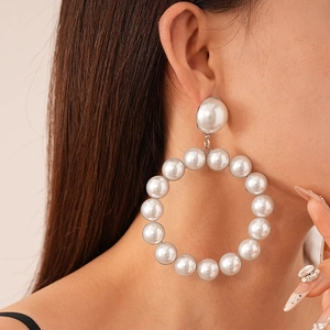 Exaggerated large geometric faux pearl hoop earrings worn by a model in a side profile view