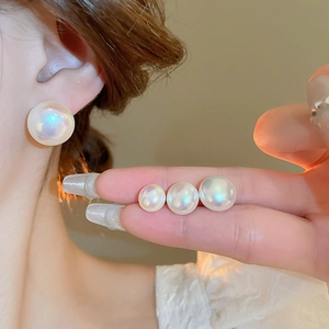 Detailed view of iridescent mermaid pearl stud earrings in multiple sizes on hand