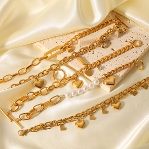 Detail of gold-plated bracelets with heart pendants and pearls on satin and travertine