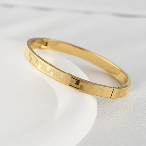 Detail of gold titanium steel bangle showing the classic Greek meander engraved pattern