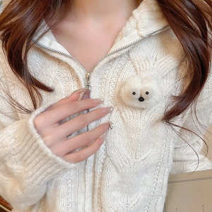 Detail of white cable knit cardigan featuring a cute plush monster brooch with a silver zipper