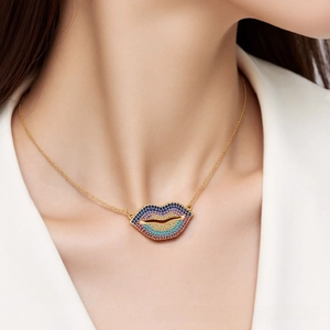 Macro detail of gold necklace with a vibrant rainbow crystal-encrusted lip pendant