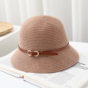 Detail of straw bucket hat featuring a brown belt strap and golden buckle on a magazine