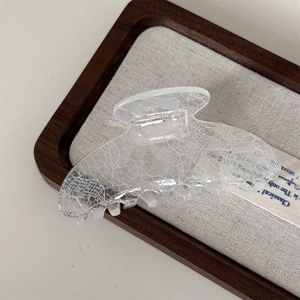 Detailed view of white lace pattern claw clip on a textured linen tray display