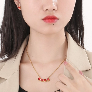 Close-up of gold titanium steel necklace and earrings set with five red zircon gemstones