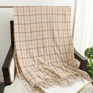 Detail view of a beige plaid tassel scarf draped over a wooden chair in cozy setting