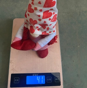 Macro shot of a red heart-themed gnome plush doll on a scale showing 41g weight