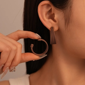 Close-up of multi-layered brown C-shaped brushed earrings worn on ear for detail