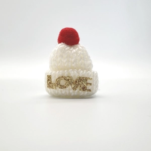 Detail einer Mini-Weihnachtsmütze aus Strick in Rot und Weiß mit goldenem LOVE-Schriftzug