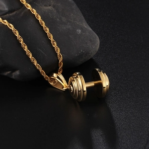 Gros plan du collier pendentif haltère doré sur pierre sombre avec chaîne torsadée