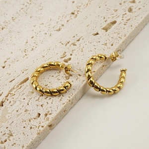 Golden titanium steel twisted rope C-shaped hoop earrings on beige stone texture