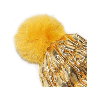 Detailed macro view of the golden metallic fabric and yellow fluffy pom-pom on the winter hat