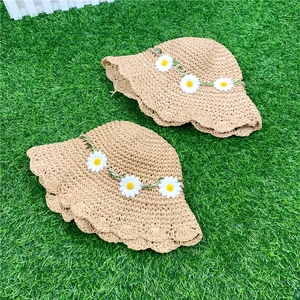Detail view of woven straw hats with floral daisy trim on green grass background