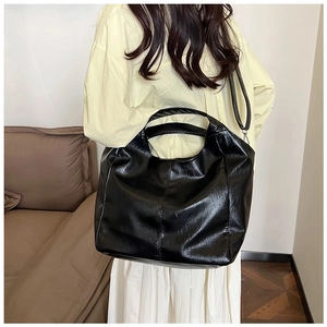 Detail of a large black leather tote bag with a high-gloss finish and adjustable shoulder strap