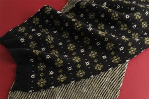 Close-up of black knitted scarf featuring yellow and white snowflake patterns on red background