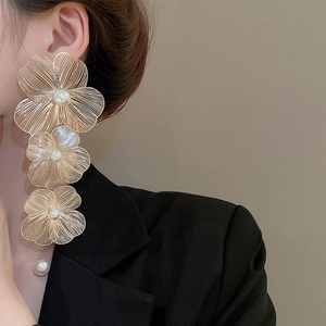 Dettaglio di orecchini a fiore dorati con perle indossati da una modella in nero