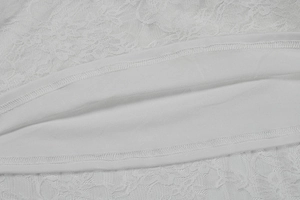 Macro detail of white floral lace texture and reinforced double-stitched hem on the dress