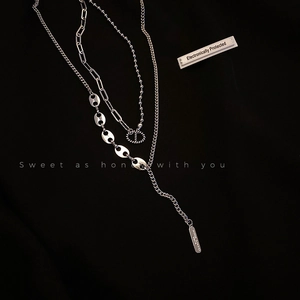 Détail macro d'un collier géométrique argenté avec pendentif CD et barre gravée