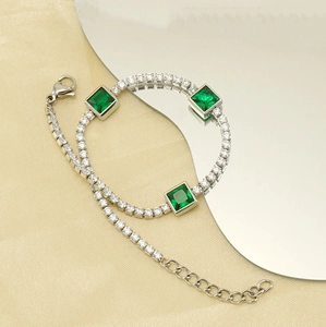Macro detail of silver tennis bracelet with green square zircons on silk background