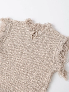 Macro detail of beige knit top featuring decorative tassels and textured woven fabric