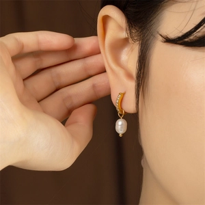 Close-up of gold U-shaped hoop earring with shimmering zircons and white pearl on ear