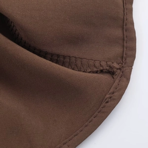 Gros plan sur la texture du tissu marron foncé et les coutures de la robe midi